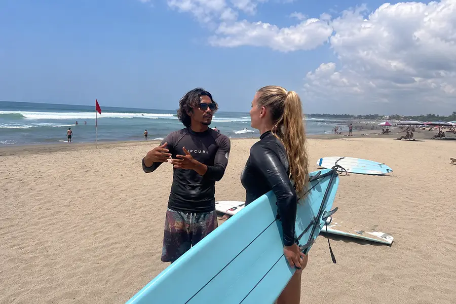A surf instructor talking to a female student holding a surfboard on the beach.