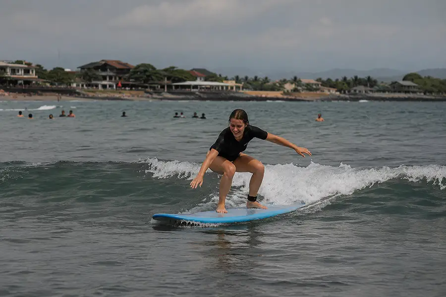 A woman balancing on a blue foam surfboard while riding a small ocean wave.