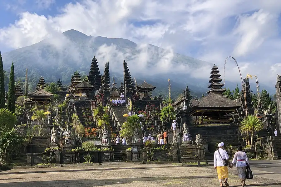 The grand stone split gate of Besakih temple in Bali, Indonesia. framing a steep staircase with the volcanic peaks of Mount Agung towering behind.