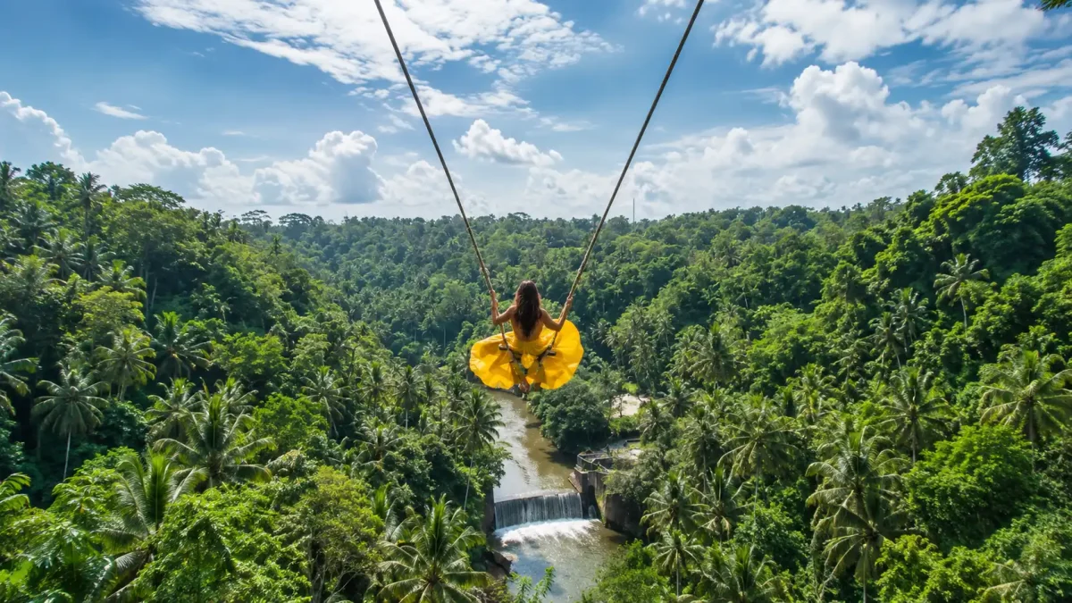 Woman in a yellow dress riding a giant swing in Bongkasa Village, Bali.