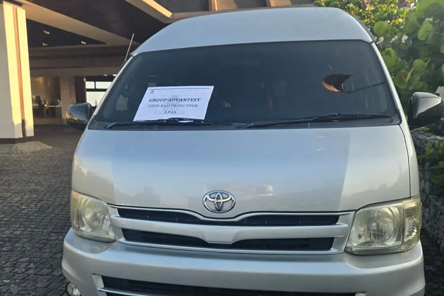 A modern airport minivan in Bali parked outside the arrivals area, featuring spacious seating, ample luggage capacity, a friendly local driver, and happy travelers ready for a comfortable and convenient airport transfer.