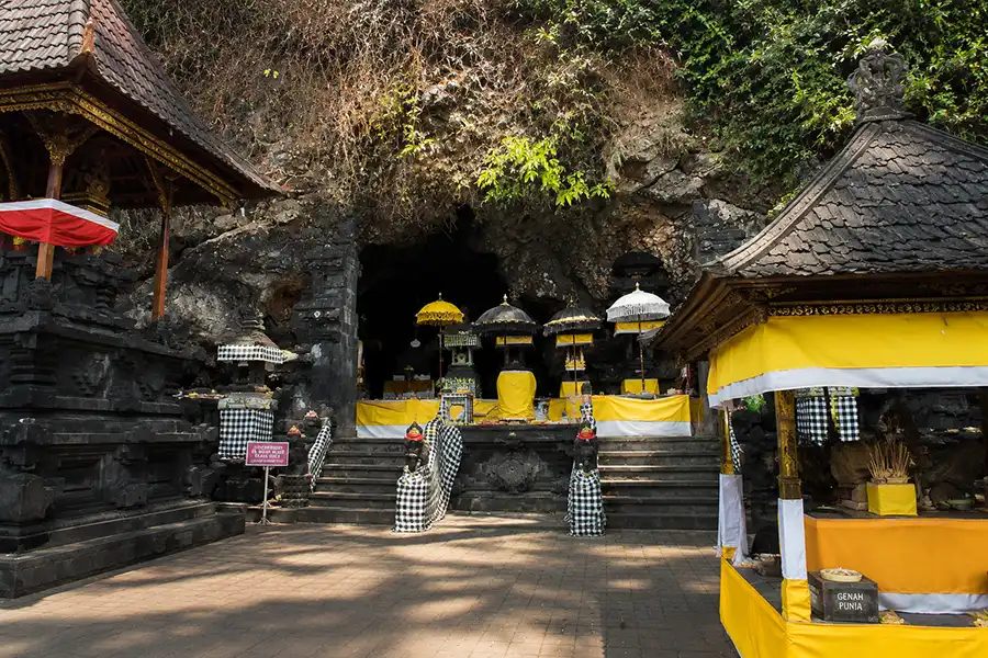 Traditional shrines and yellow ceremonial umbrellas built directly at the mouth of a large cliffside cave.
