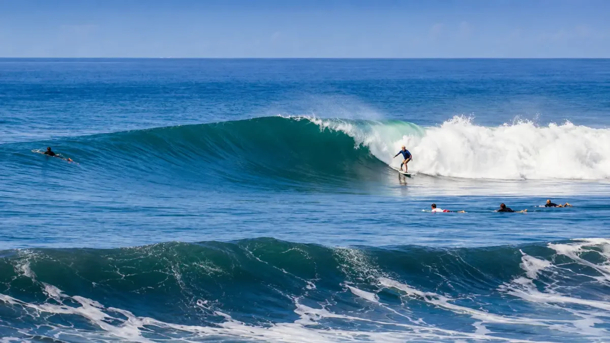klotok beach - klungkung interesting places to visit - bali touristic Surfers riding waves at Klotok Beach with black sand and scenic coastline in Bali.
