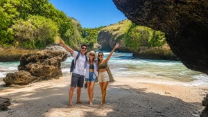 Tourists enjoying the peaceful shoreline of Lumangan Beach with crystal-clear water and dramatic coastal cliffs in Bali.