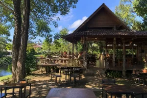 A traditional wooden restaurant pavilion with a thatched roof surrounded by shade trees.