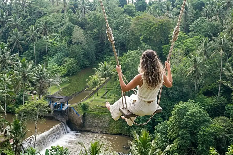 A woman soaring high on a rope swing over a river dam and dense tropical jungle.