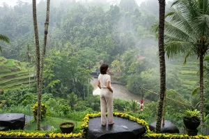 A woman standing on a large stone deck looking out at a foggy jungle valley and river.