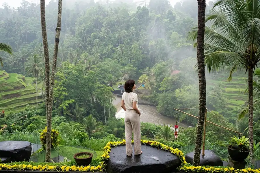 A woman standing on a large stone deck looking out at a foggy jungle valley and river.