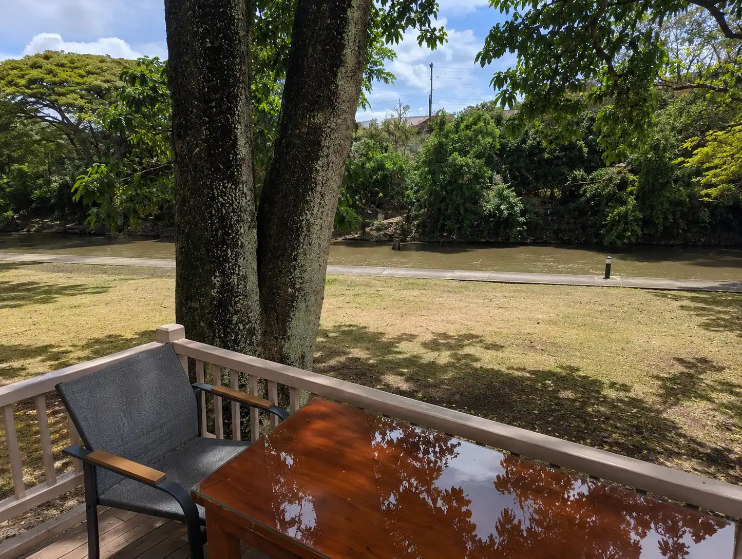 An outdoor wooden dining table and chair overlooking a calm river and green trees.