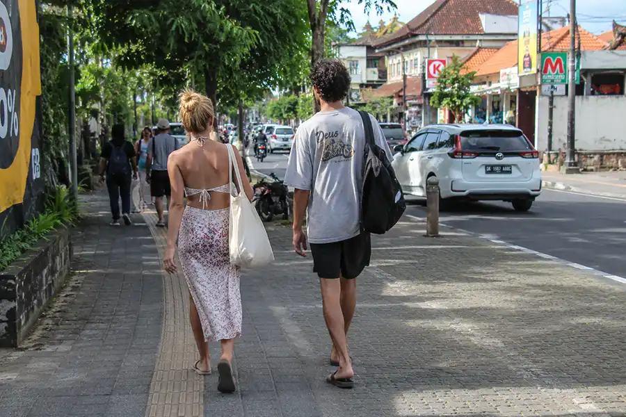 A man and woman walking down a paved sidewalk in casual streetwear, showcasing comfortable and simple travel outfits in bali.