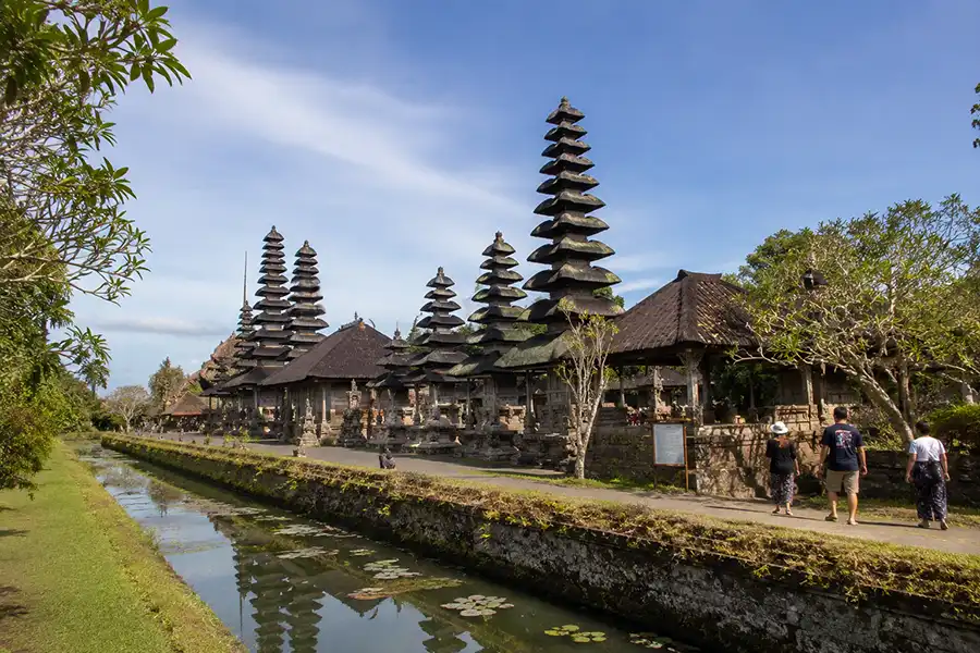 A row of multi-tiered thatched roofs reflecting on a calm water moat running alongside a grassy garden pathway.