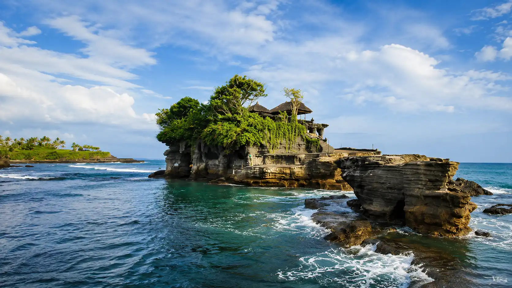 Scenic view of Tanah Lot Temple surrounded by crashing waves at sunset in Bali.