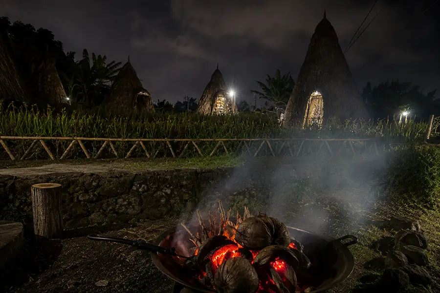 A glowing campfire at night with traditional thatched huts at Maha Gangga Valley.