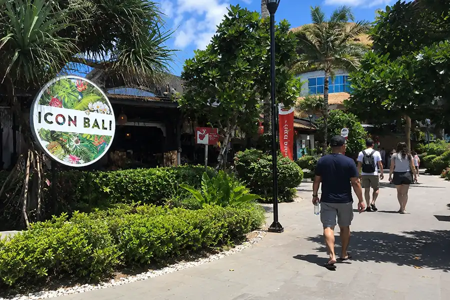 A paved walkway surrounded by palm trees and greenery outside Icon Bali Mall Sanur.