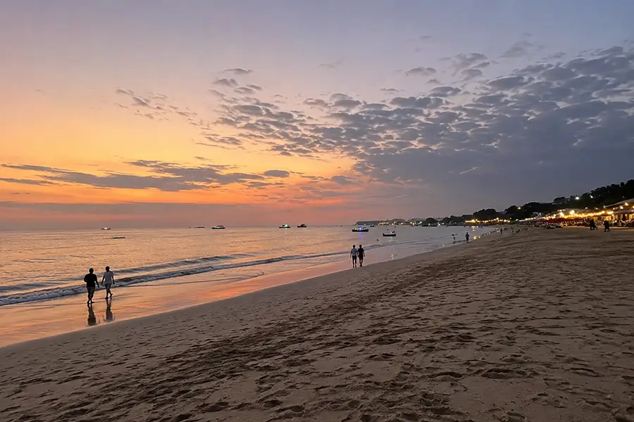 People relaxing on colorful beanbags on a wide sandy shore watching the sunset over the ocean.