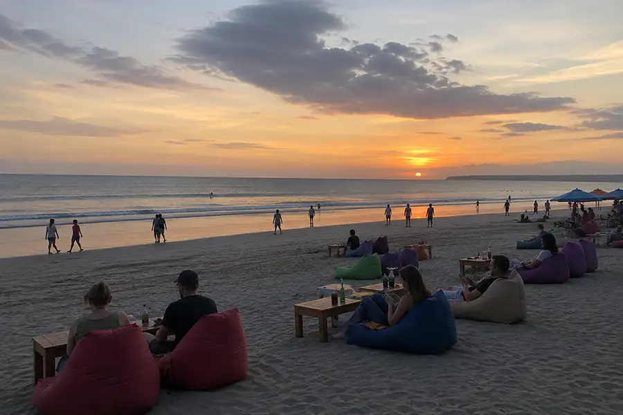 People relaxing on colorful beanbags on a wide sandy shore watching the sunset over the ocean.