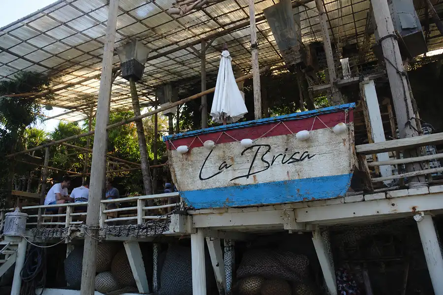 A rustic wooden beach club venue featuring a decorative boat sign with the text La Brisa.