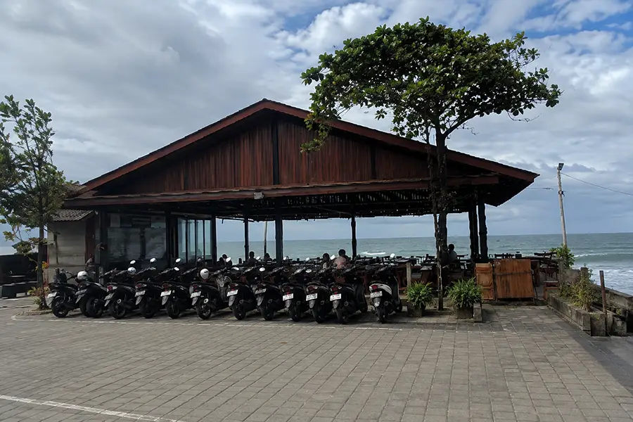 A line of parked scooters next to an open-air oceanfront wooden pavilion overlooking the sea.
