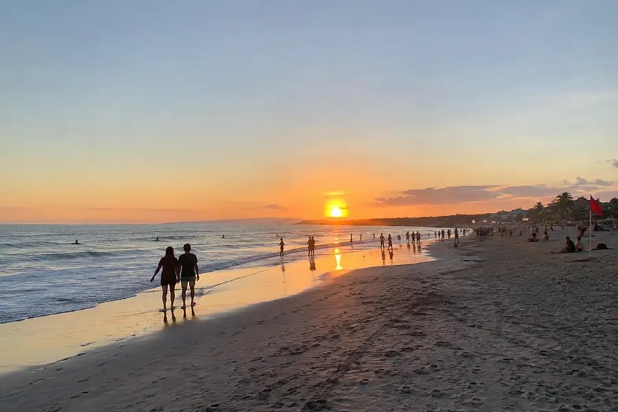 People relaxing and walking on the beach while watching a golden sunset over the ocean.