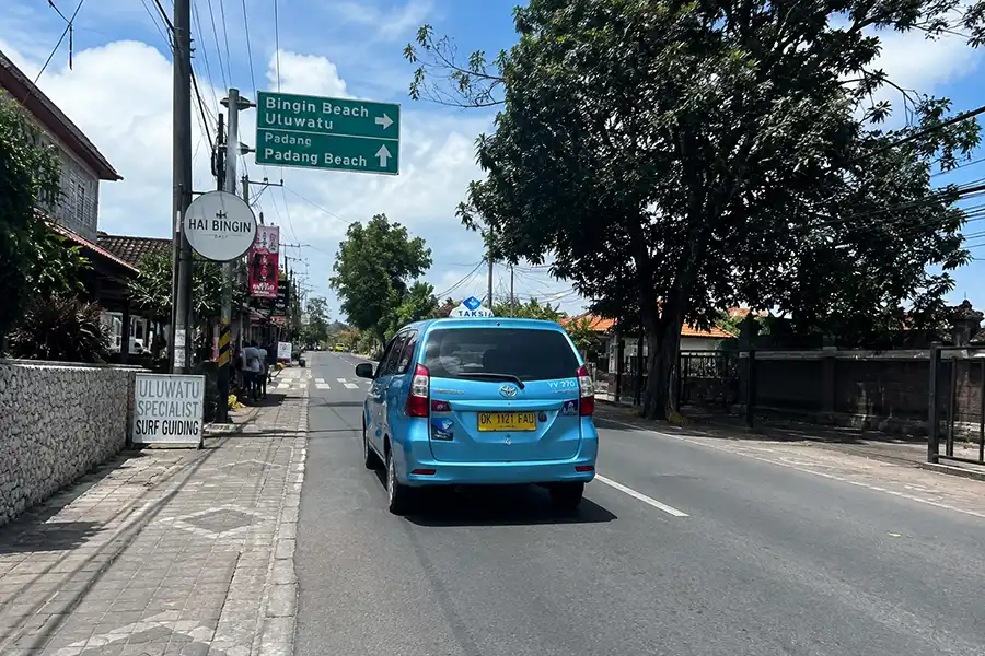 Blue taxi passing road signs on the way from Bingin to Uluwatu.