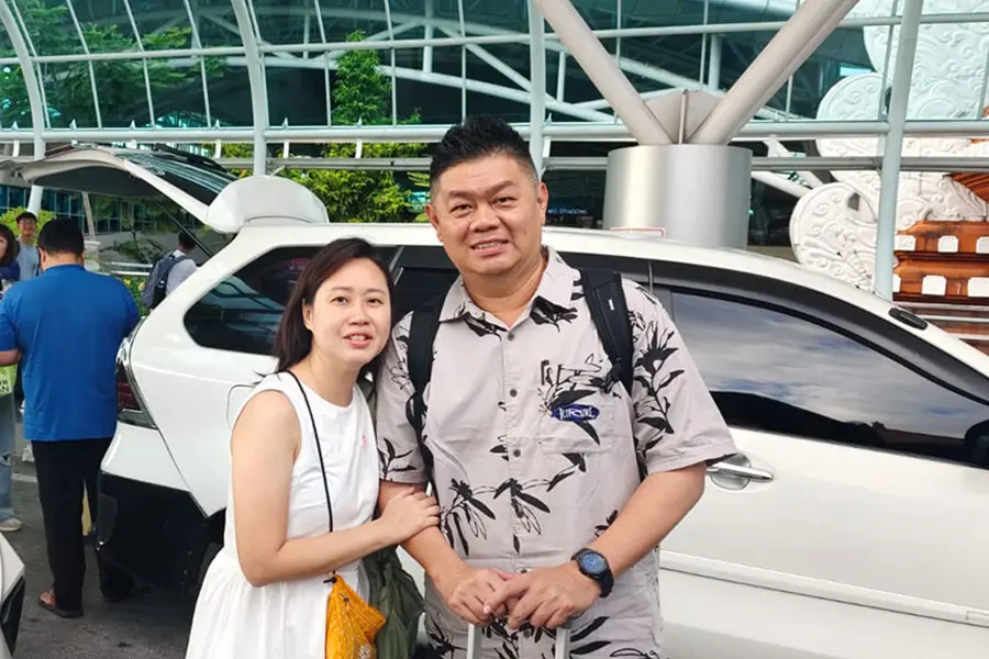 A couple posing together in front of a white private transport vehicle outside the airport.