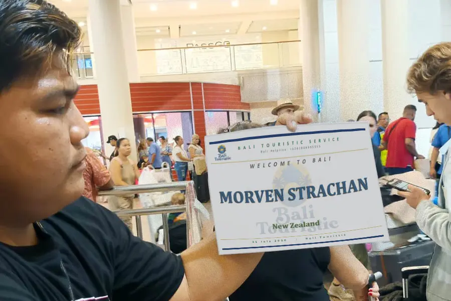 A driver holding up a personalized printed name sign at the busy airport arrival hall.