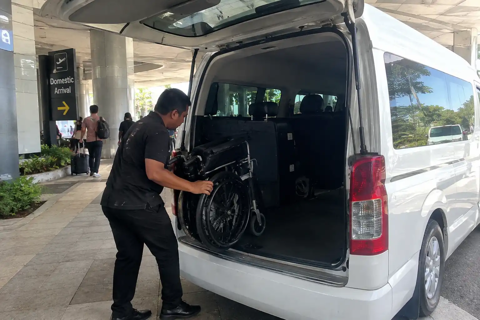 Folding wheelchair being loaded into a Bali airport transfer vehicle